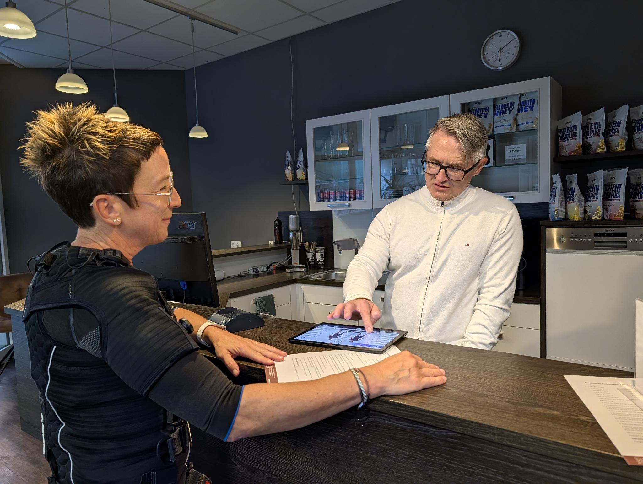 Trainer bespricht mit einem Mitglied den Trainingsplan am Tablet